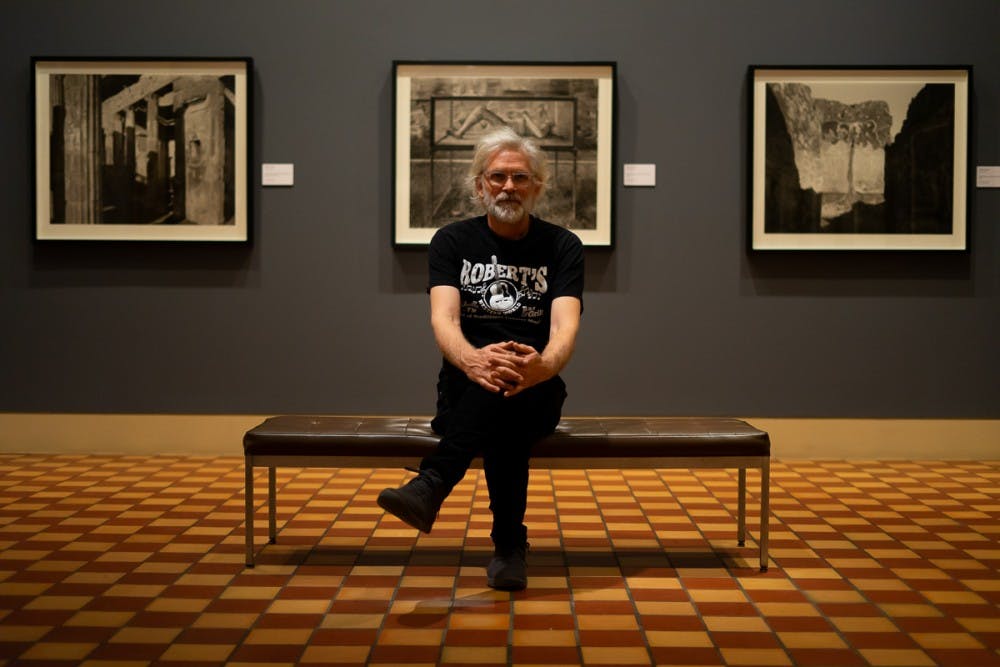<p>Professor William Wylie sits in front of his photo exhibit, currently on display at the Fralin Museum of Art.</p>