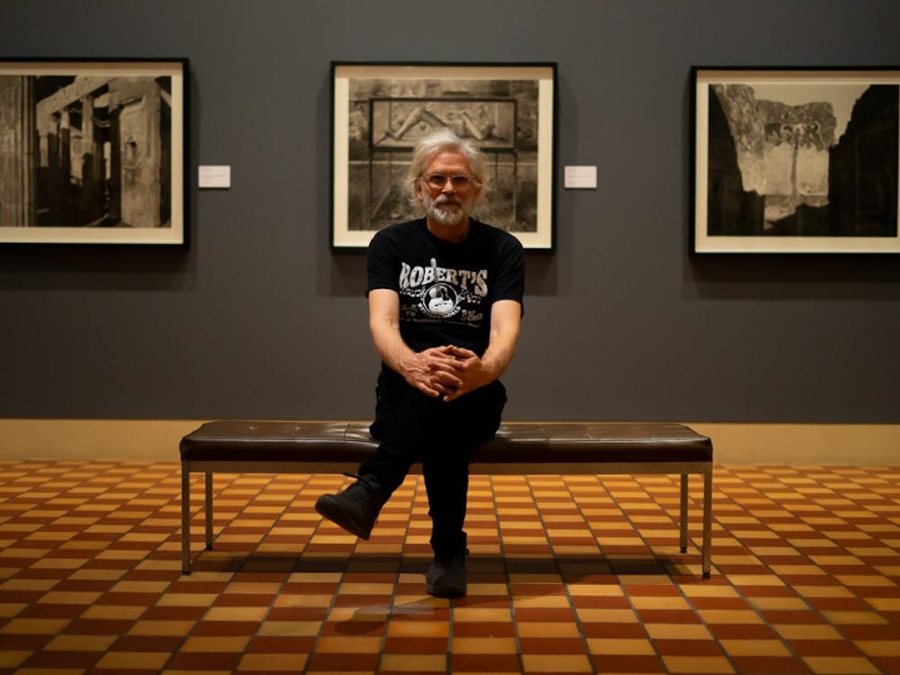 Professor William Wylie sits in front of his photo exhibit, currently on display at the Fralin Museum of Art.