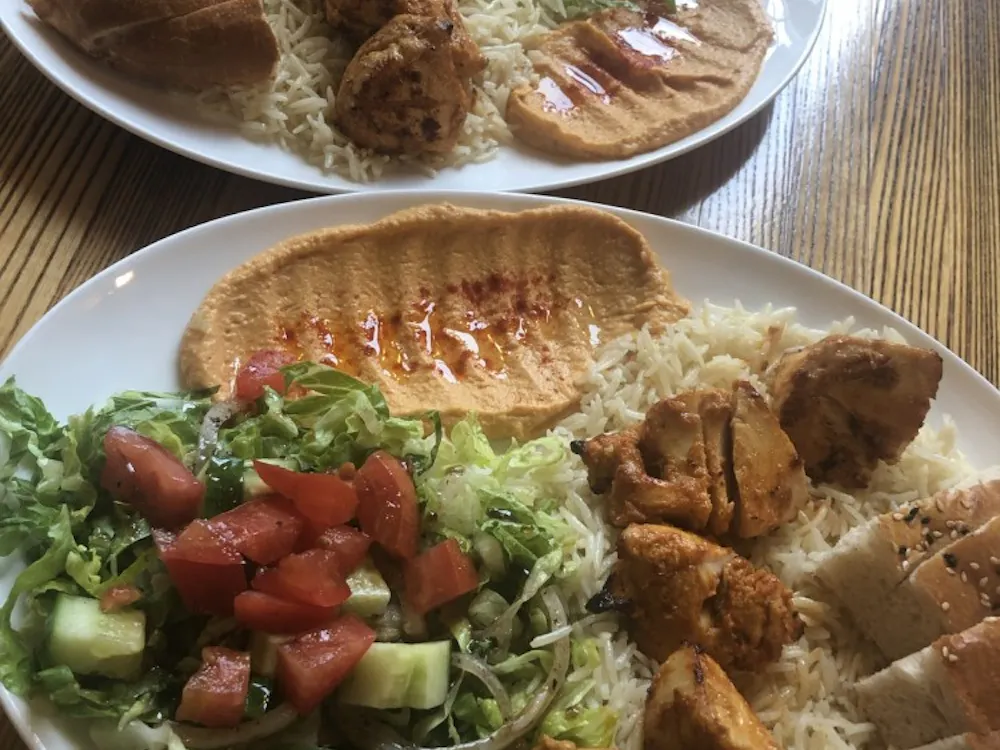The Chicken Shish Kebab Platter consists of skewered pieces of grilled chicken breast, served with rice, salad, hummus and homemade pita bread. 