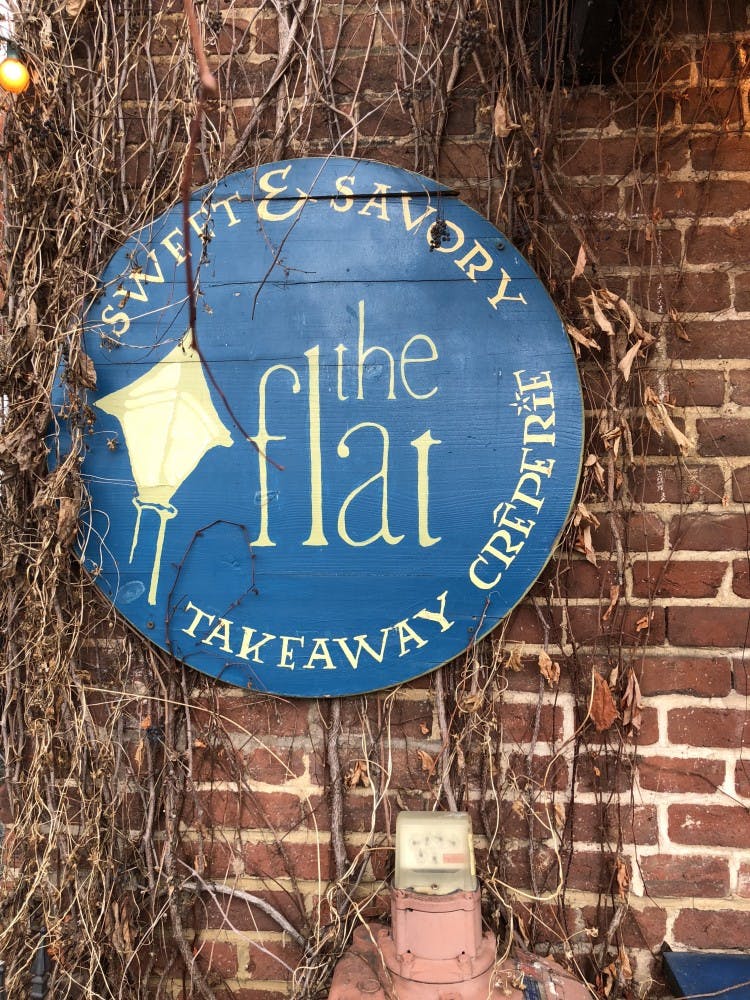 The Flat’s brick exterior, crawling with ivy and strung with colored lights, lends a cozy and inviting atmosphere to the outdoor seating area.