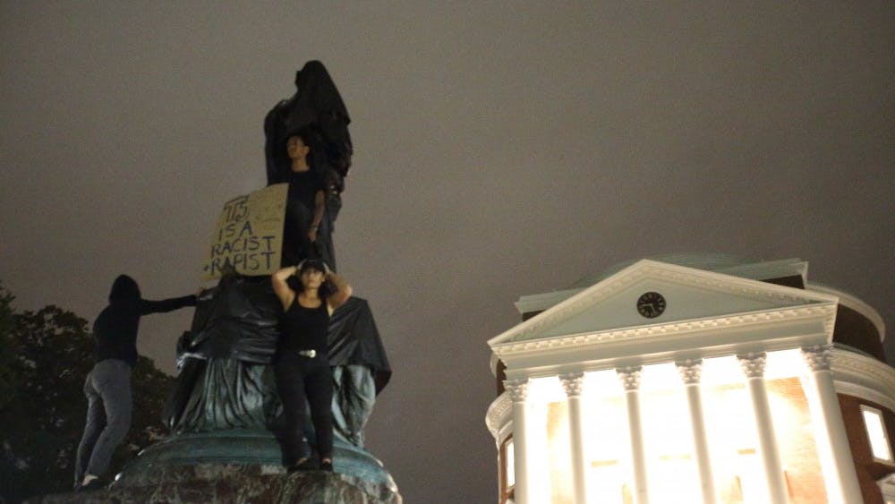 Protesters stand atop the statue of Thomas Jefferson statue north of the Rotunda after shrouding it.&nbsp;