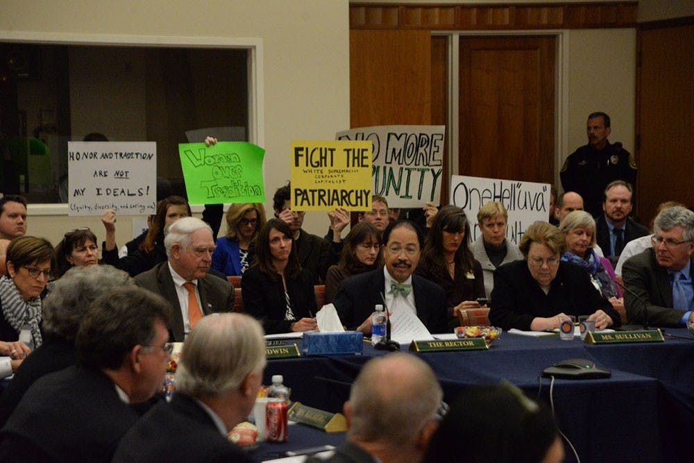 Audience members hold signs in protest during the Board meeting.