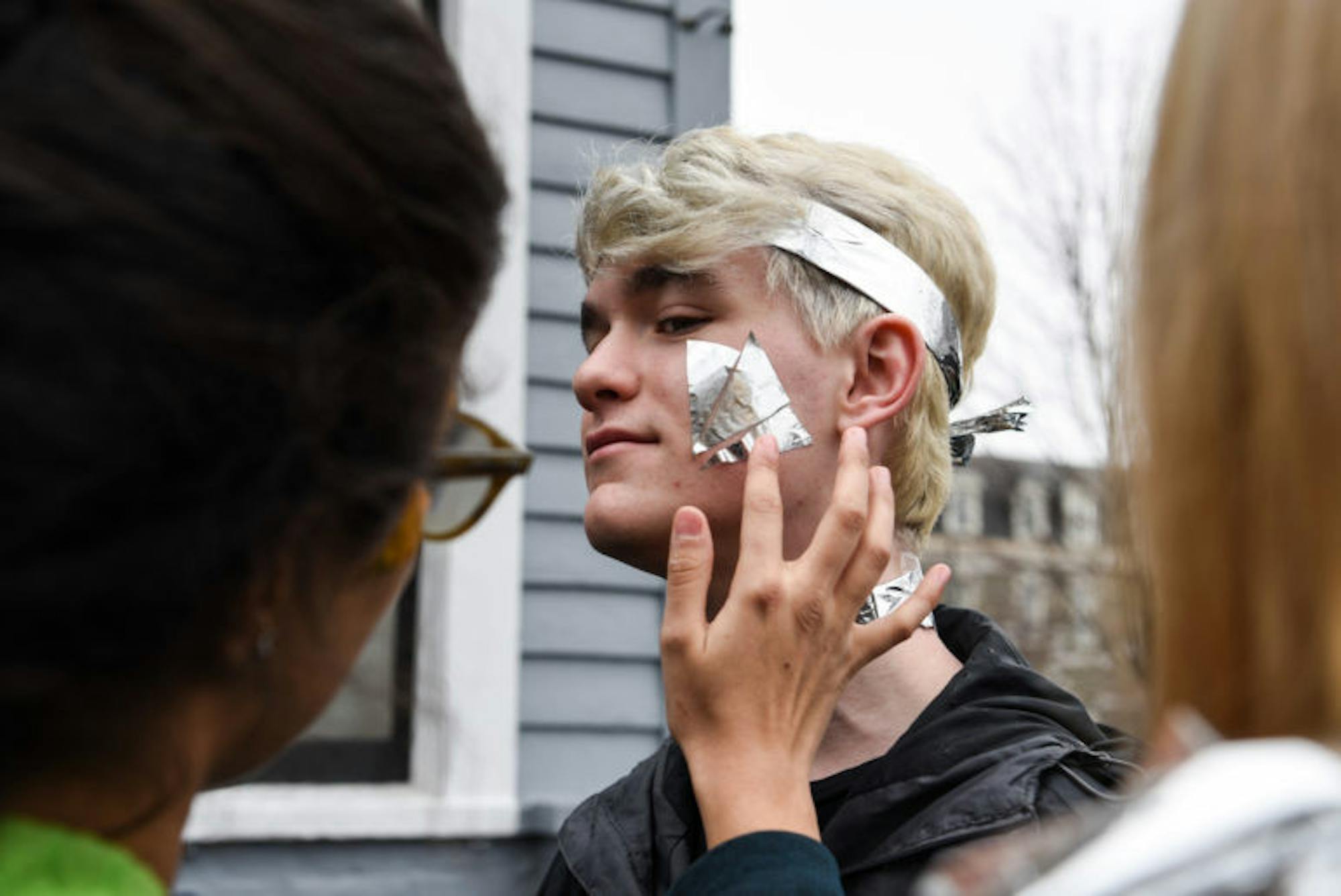 A classmate helps Walter Collins ’22 paste pieces of reflective mylar sheets onto his face as he prepares for the parade. The material was primarily used in the dragon’s scales but was also incorporated into the first-year students’ costumes.