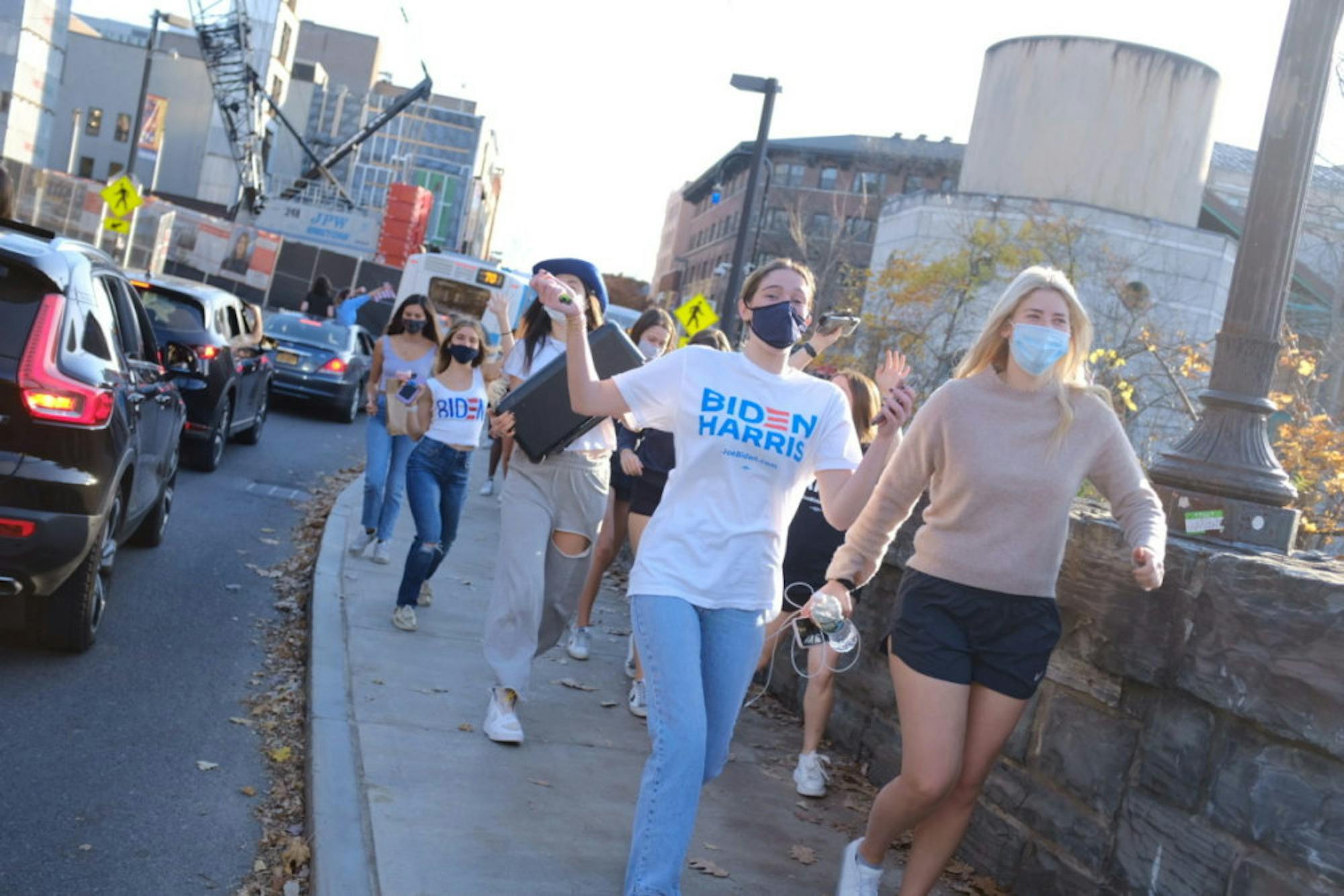 Students skip down the Collegetown sidewalk on Saturday as they celebrate the Biden-Harris win.