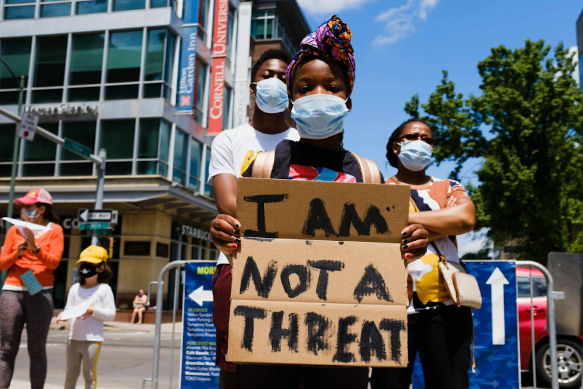Donning a mask, a child holds up a cardboard sign that reads ‘I Am Not a Threat’ during the Uplift and Speak Out! rally on Friday at the Ithaca Commons. (Michael Suguitan / Sun Staff Photographer).