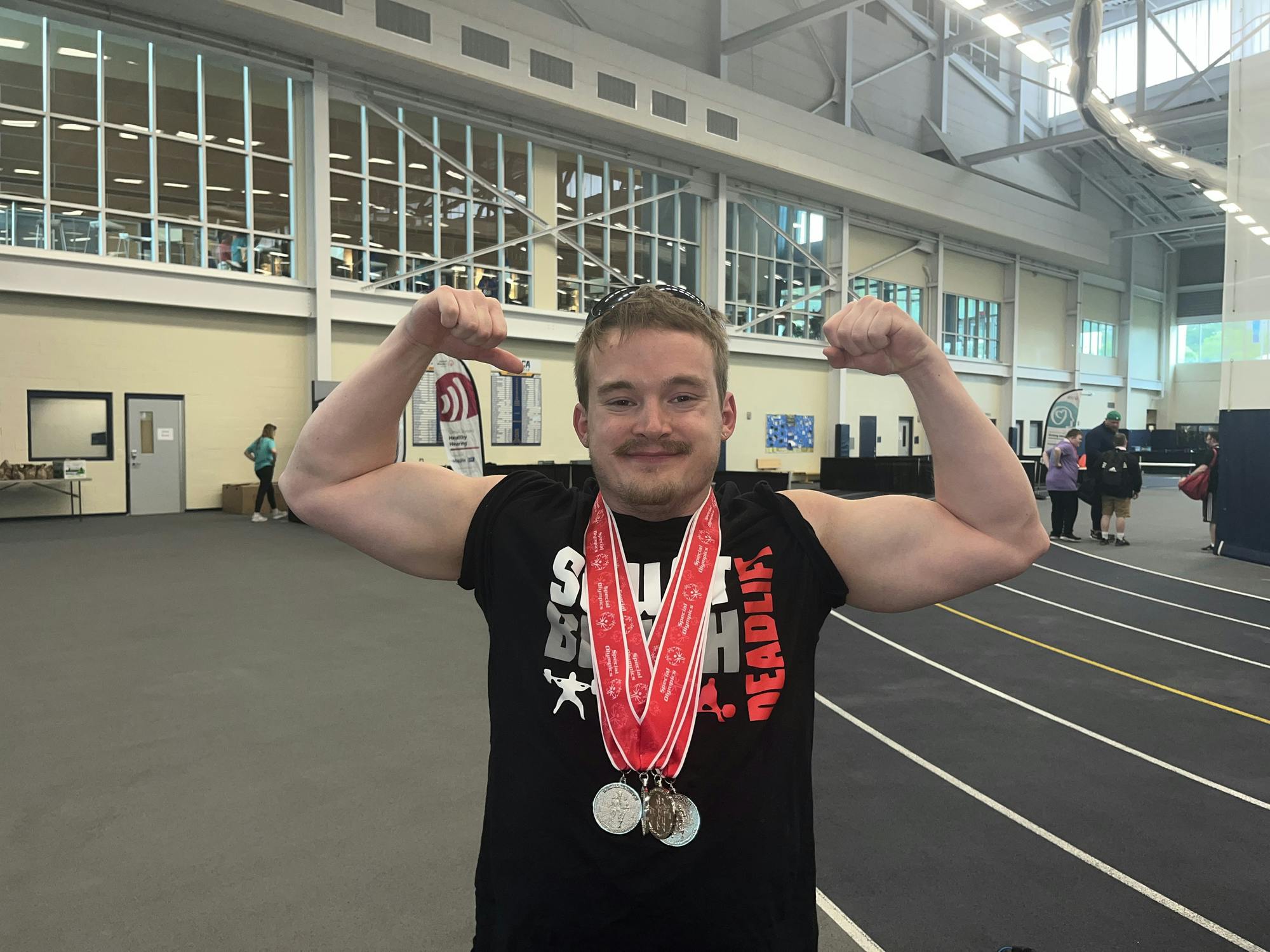 Ryan Ruvola flexes with his medals after lifting over 400 pounds in the powerlifting competition.