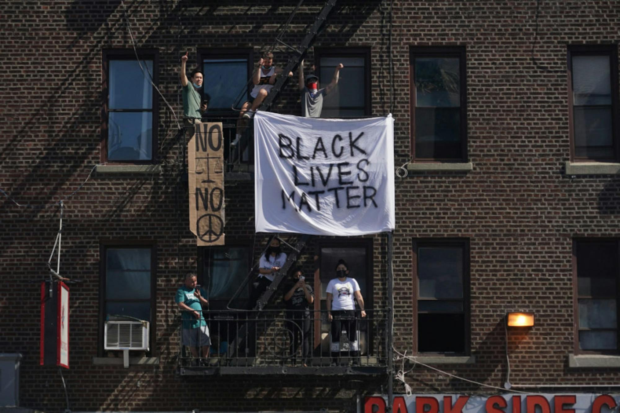 Onlookers hang signs from a building's fire escape as demonstrators crowd a nearby intersection as they protest the death of George Floyd and police brutality on May 30 in New York City.
