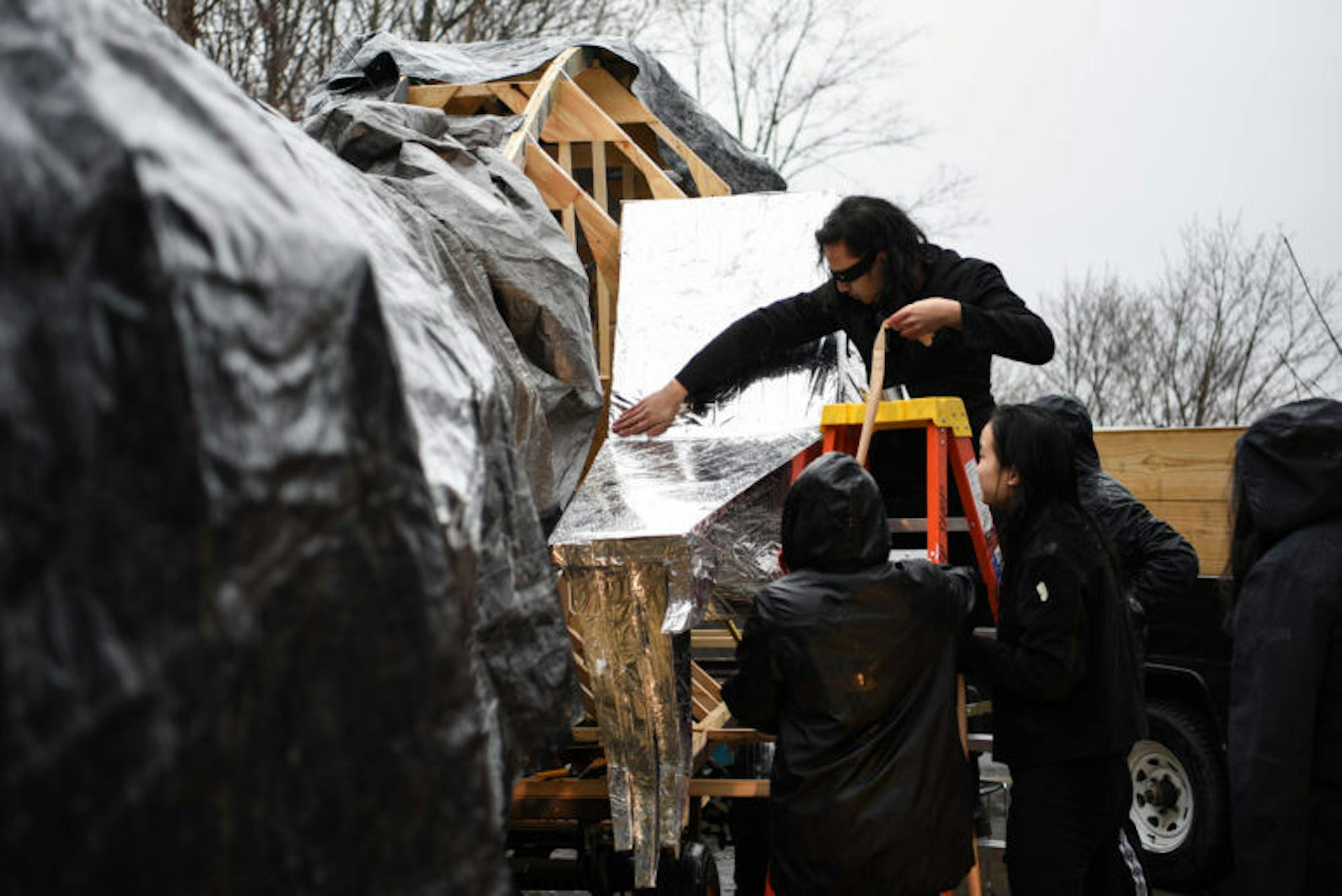 Francis Encarnacion ’22 (standing on the ladder) puts the finishing touches on the right leg of the dragon. Although the rain continued into the morning, students resumed construction on some parts of the dragon; a tarp was draped over the remaining sections to prevent water damage.