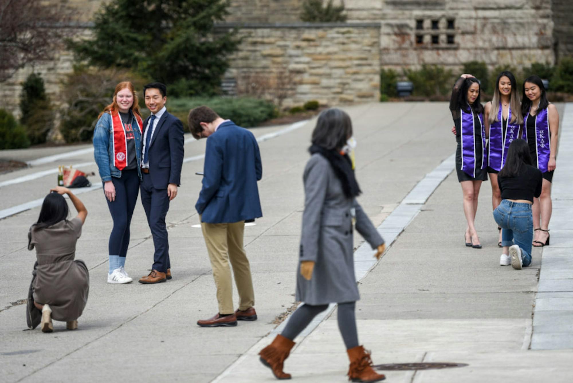 Students take portraits on Ho Plaza as a woman wearing an N95 respirator walks past on March 18, 2020. Many seniors took advantage of the class suspension to take graduation photos on campus.
