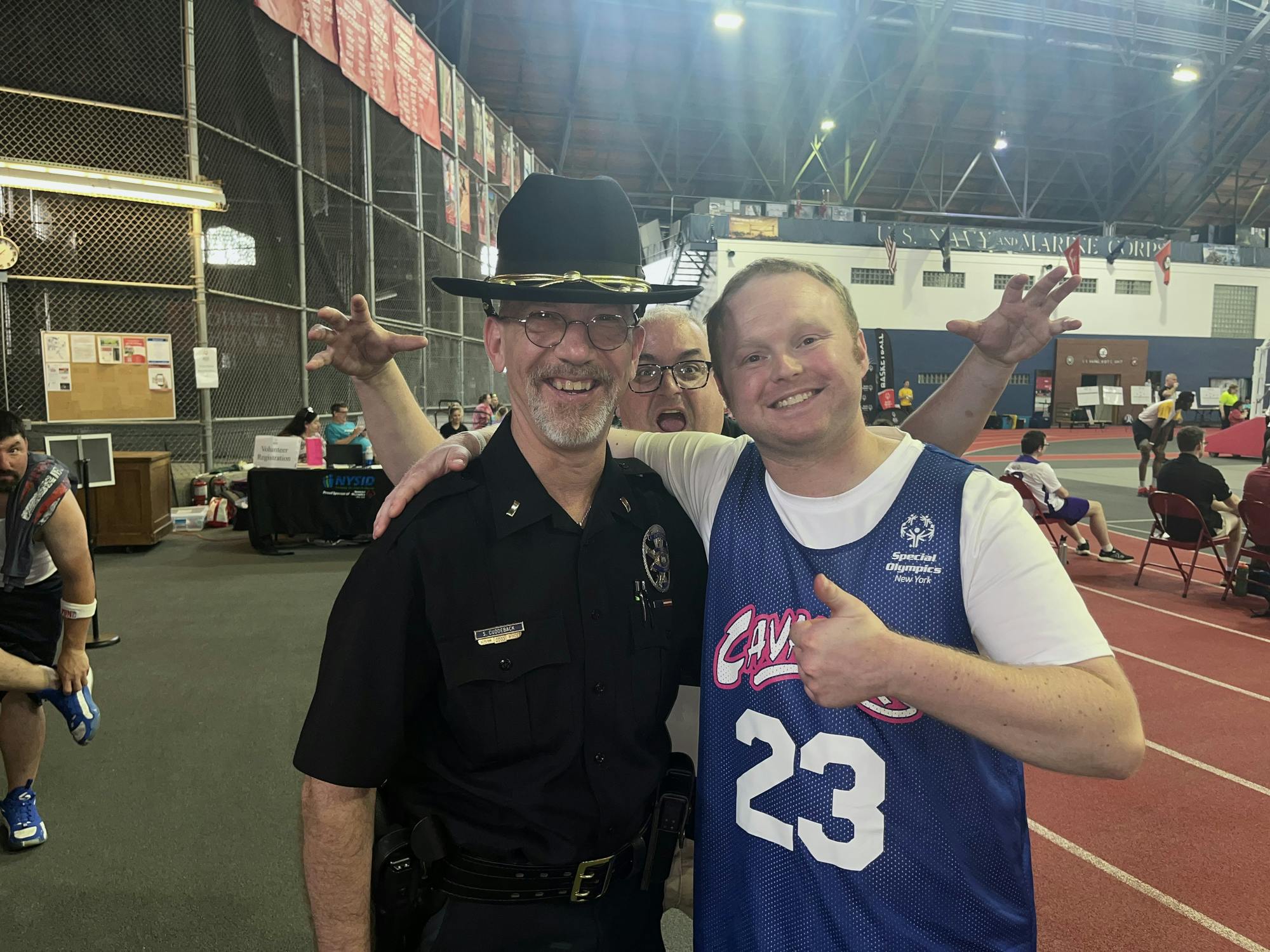 Jacob Babcock smiles beside Officer Shaun Cuddeback. Babcock’s coach photobombs the duo from the back.
