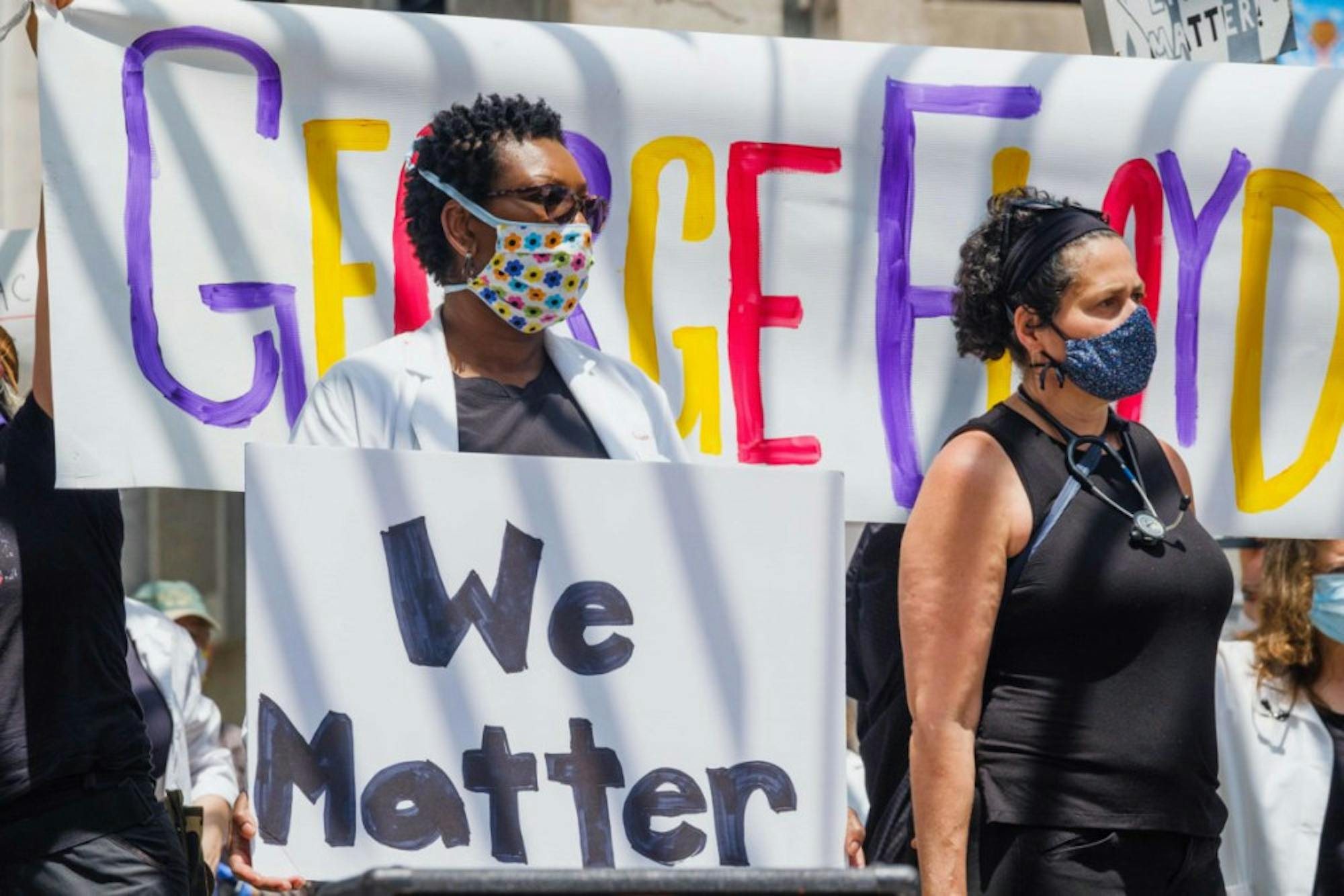 A hand-painted sign with George Floyd's name hangs behind participants. (Michael Suguitan / Sun Staff Photographer).