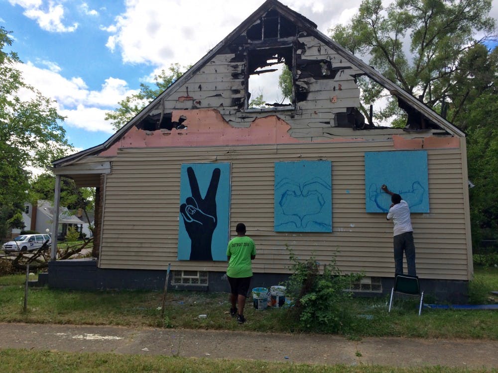 <p>Former DIT student Samuel Bessiake paints murals on an abandoned house across from the entrance to Cody DIT about a month before the house was torn down. A neighbor stopped the crew and asked them to save the murals, which were moved to another vacant house.</p>