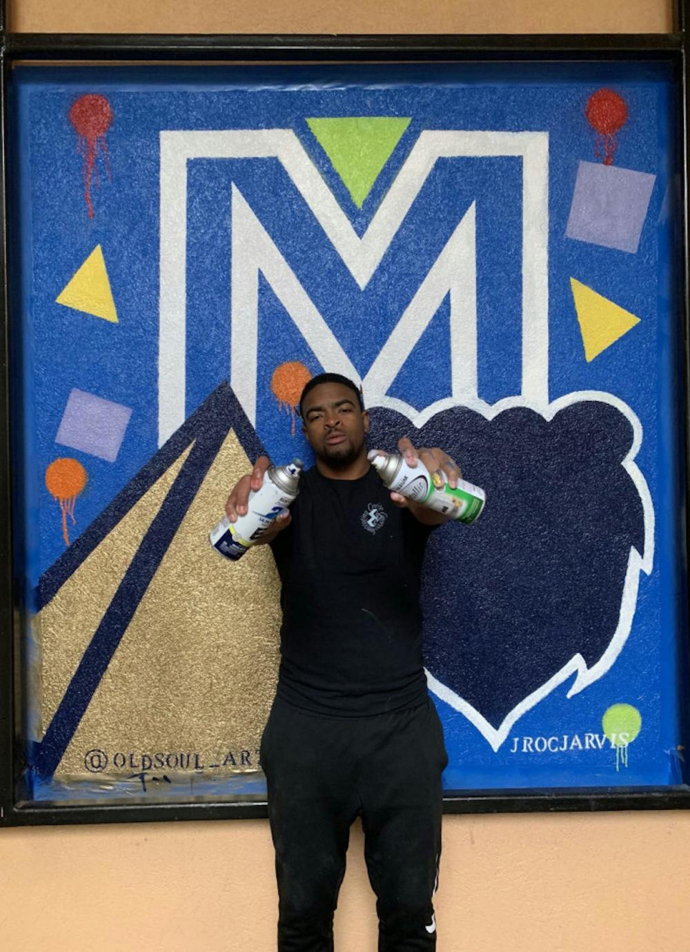 <p class="p1"><span class="s1"><strong>UofM senior, Jarvis Howard, posing behind an abstract mural he spray-painted as commissioned by Oak Court Mall.</strong></span></p>