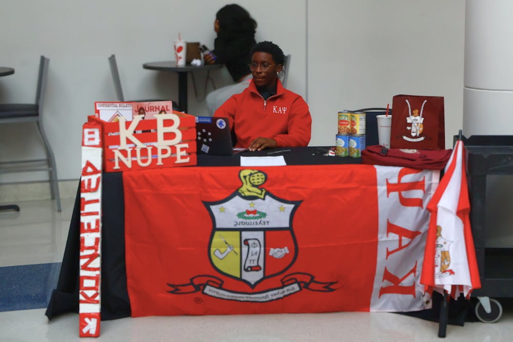 <p>A member of Kappa Alpha Psi Fraternity Inc. sits at a table in the University Center during the fraternity’s canned food drive on Wednesday.</p>