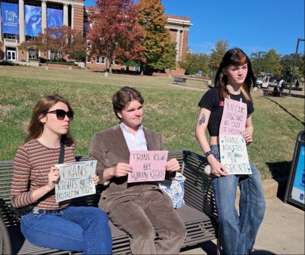 <p>Protesters sit on a bench outside the University Center Alumni Mall holding signs in support of transgender rights during a demonstration against a Turning Point USA tabling event on Tuesday.</p>