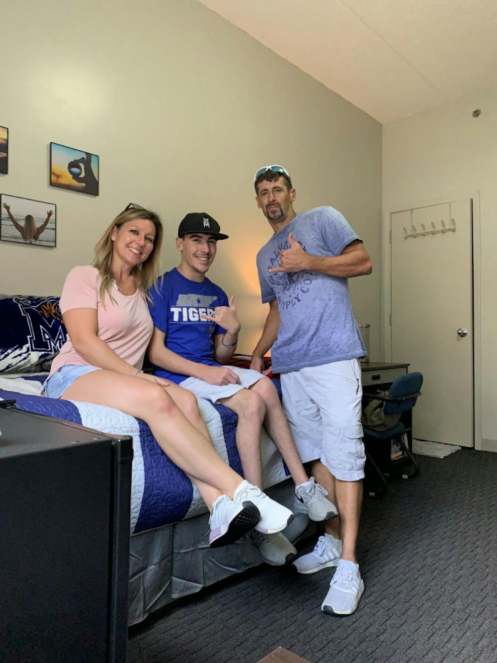 <p>Logan Bomar, center, sits on his dorm bed after moving in for his freshman year at the University of Memphis. To his right is his mother and to his right is his father.</p>