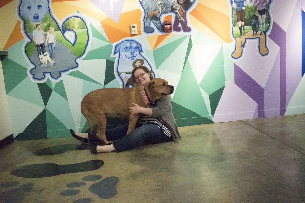 <p>Katie Pemberton hugs Sweetie, a dog kept in the office who is suspected of having heartworms. They sit in front of the new mural which shows people and animals all across Memphis.</p>