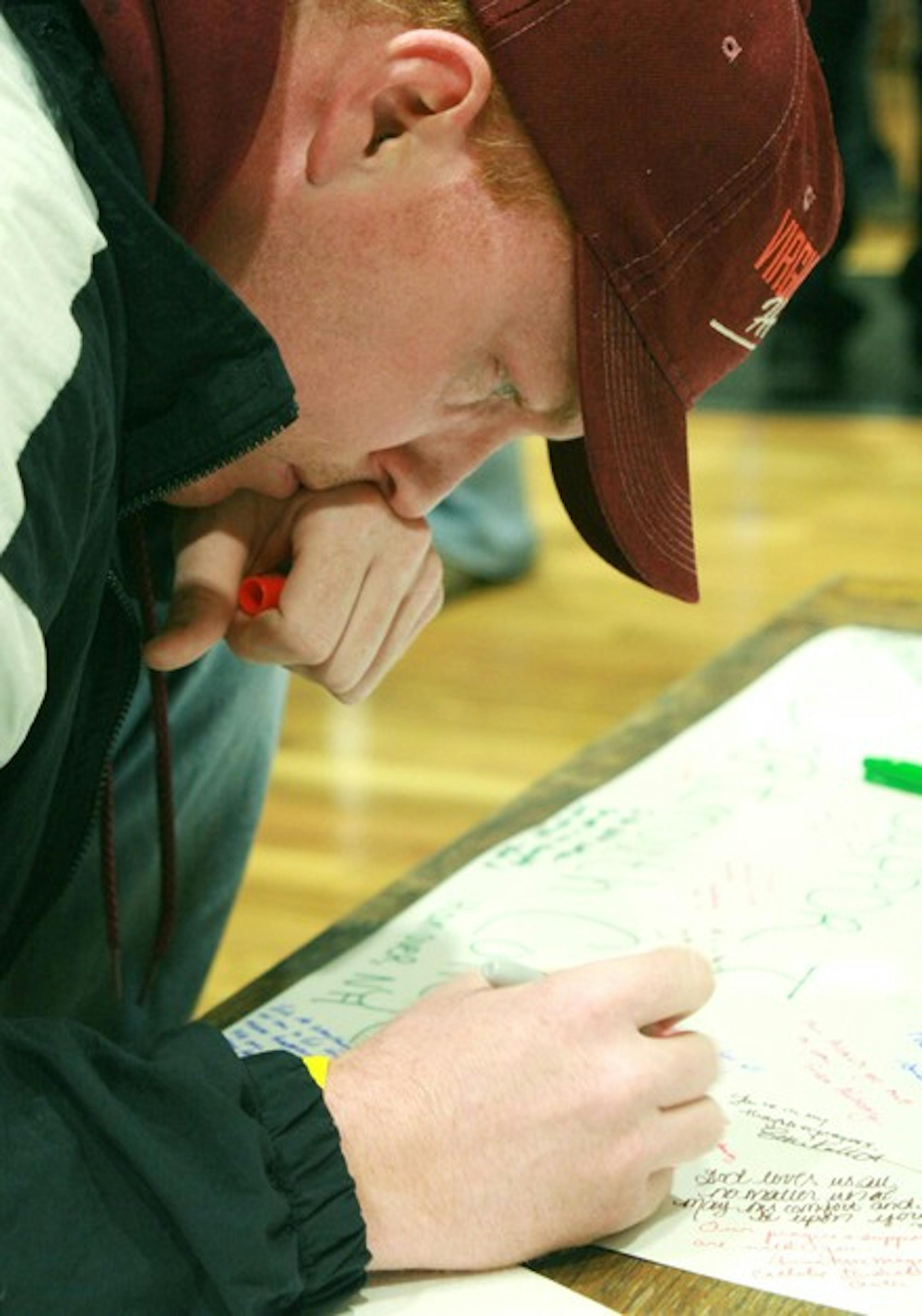 A participant in Monday night's vigil ceremony, sporting a Virginia Tech hat, signs a giant card in Collis Cafe. It will be sent to the university Wednesday.