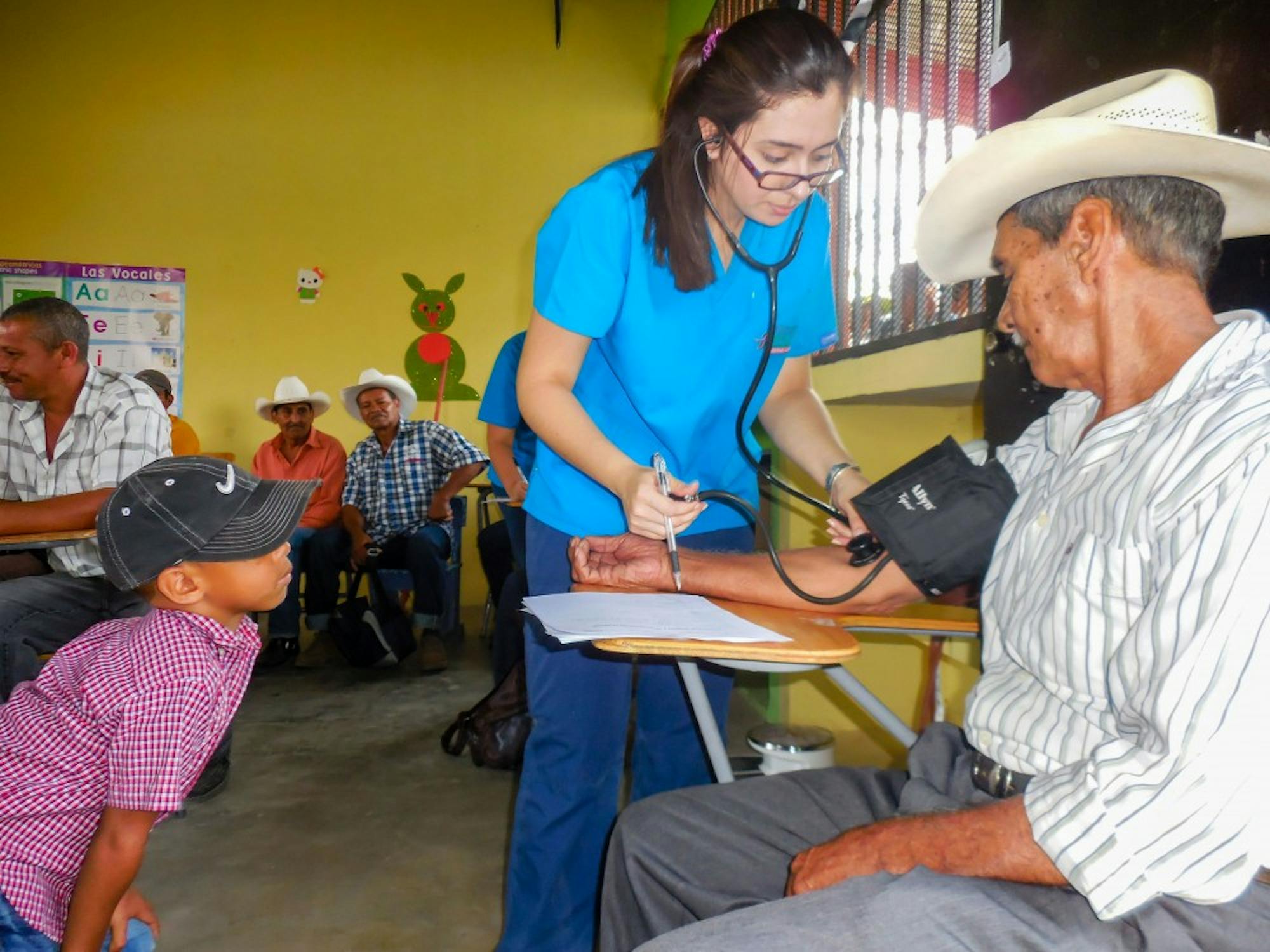 A 'Pesca' volunteer takes the blood pressure of one of the Jornada participants while his grandson watches during the May 2017 Jornada in El Rosario, Honduras.