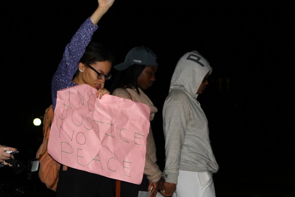 A protestor holds a sign at the East Campus bus stop, where a student march ended Monday night and the participants gathered to sing and chant.