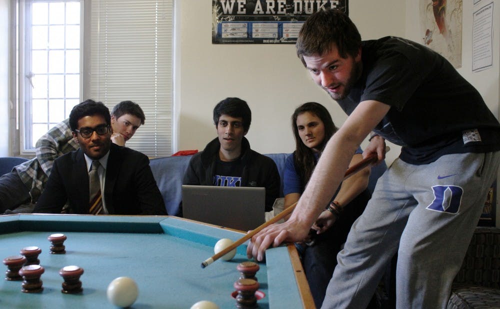 Tyler Glass shoots a bumper pool ball in his dorm room as spectators look on.