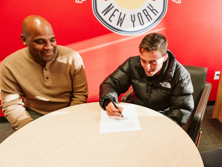 Peter Stroud signs his contract alongside New York Red Bulls sporting director Denis Hamlett.