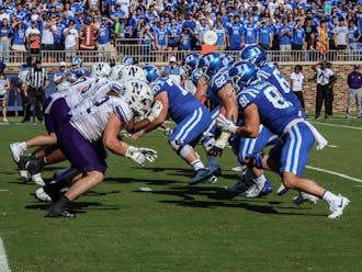Duke's offensive line rushes forward to block Northwestern's defense.