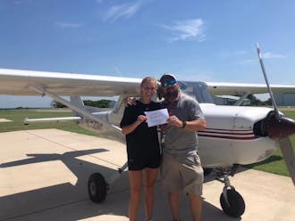 Sydney Simmons standing with her FAA examiner, holding her new private pilot certificate.