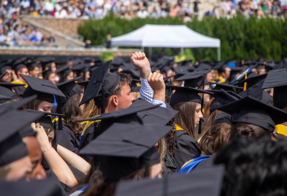 <p>Graduates looking towards stage with hands raised above the crowd.</p>