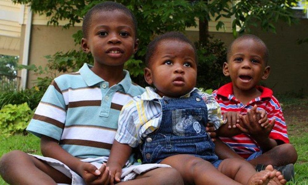 Three children sit on the grass in front of the Genesis Home