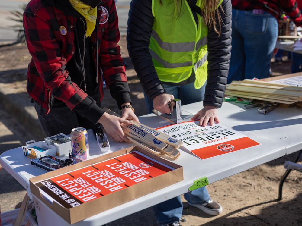 <p>Two protestors collaborate to staple signs and hand them out to people in the crowd.</p>