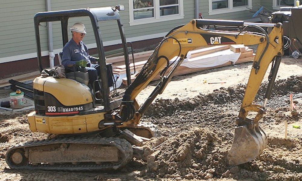 Construction workers plow the grounds outside Mill Village Wednesday afternoon. Although the interior of the new buildings are finished, this winter’s inclement weather caused significant delays in the construction of the areas surrounding the new building.