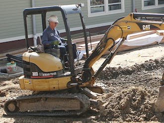 Construction workers plow the grounds outside Mill Village Wednesday afternoon. Although the interior of the new buildings are finished, this winter’s inclement weather caused significant delays in the construction of the areas surrounding the new building.
