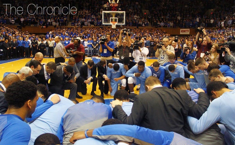 Duke and North Carolina kneeling at midcourt prior to their 2015 matchup, honoring legendary Tar Heel head coach Dean Smith less than two weeks after his death.