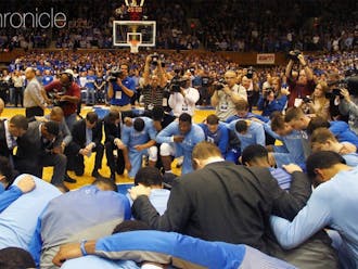 Duke and North Carolina kneeling at midcourt prior to their 2015 matchup, honoring legendary Tar Heel head coach Dean Smith less than two weeks after his death.