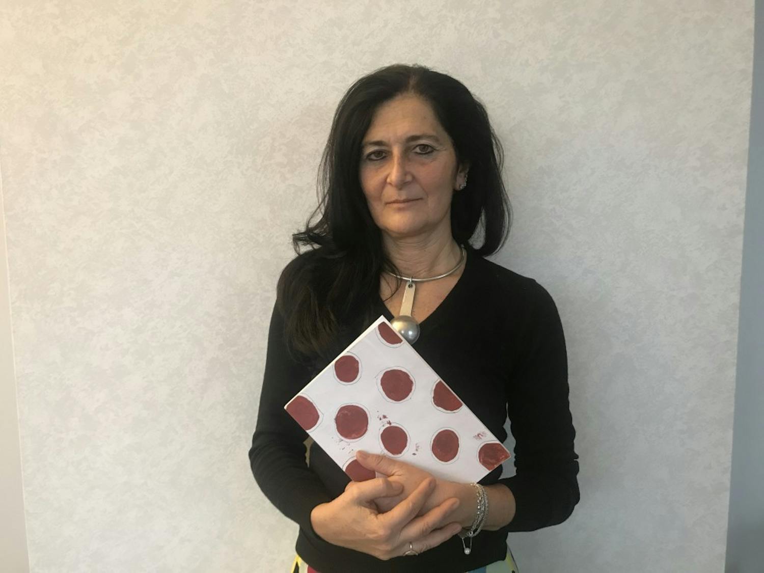 Manuela De Leonardis poses with her book ‘The Blood of Women: Traces of Red on White Cloth’ after her lecture at the FedEx Global Education Center. 

