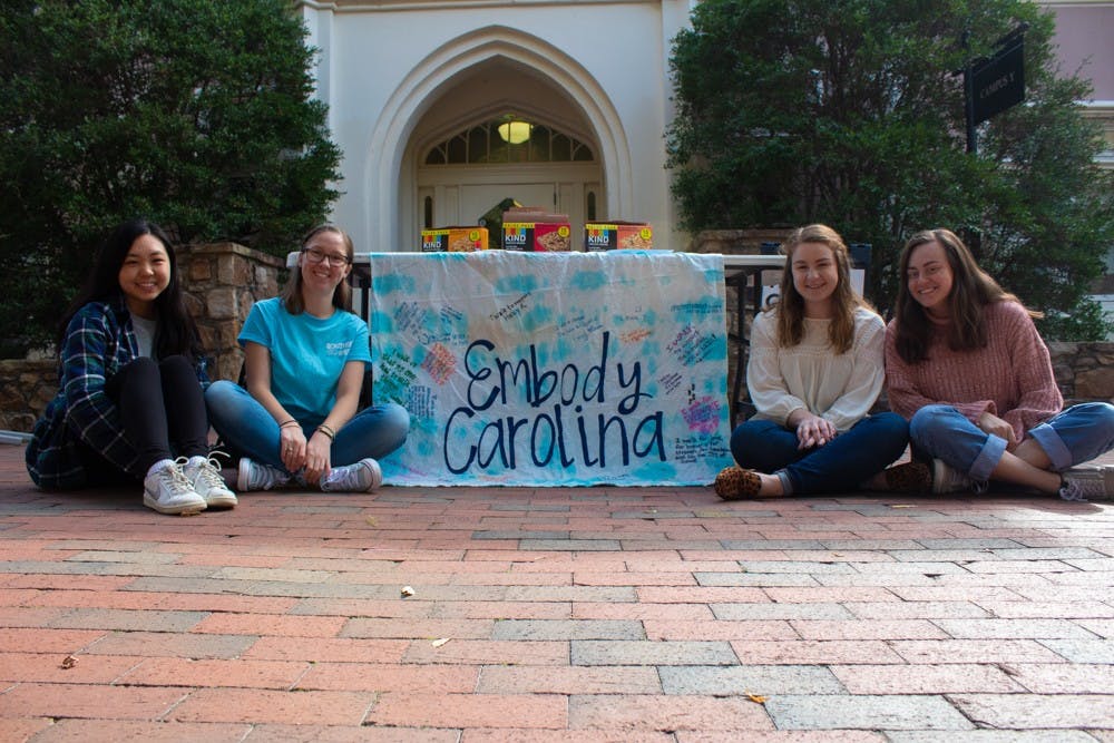 (From left ) Grace He, a junior music and psychology major; Cameron Lynch, a sophomore undecided major; Ashley Broadwater, a senior public relations major; and Maya Wahl, a junior exercise and sport science major, pose in front of an Embody Carolina banner in front of the Campus Y on Monday, Nov. 4, 2019.