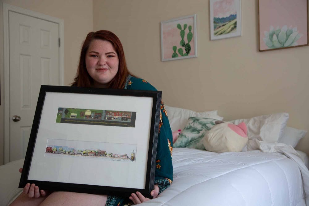 <p>Ashlin Elliott, a senior majoring in media and journalism, holds up a picture of her hometown, Columbia, NC, in her house in Carrboro, on Saturday, Sept. 29, 2019. &nbsp;Elliott says that she realized that she had some gaps in her education compared to her peers who come from other parts of the state.</p>
