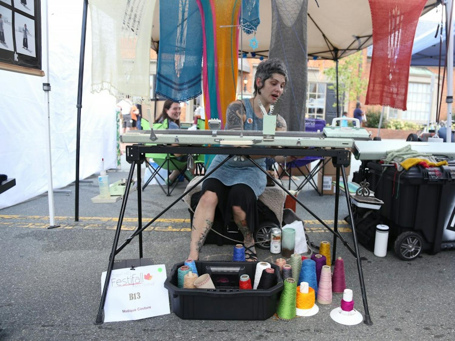 &nbsp;
Raleigh-based artist, Eris Swanstrom, knits on a knitting machine at her booth at Festifall, a Chapel Hill festival &nbsp;&nbsp;showcasing local artists. The celebration of art is held annually in Downtown Chapel Hill, this year falling on Sunday. Swanstrom knits on her vintage, special-edition knitting machine as shoppers peruse her racks of skirts, shirts, mittens and other knitted wool garments. Modique Couture, Swanstrom’s business, features one-of-a-kind wearable pieces of art. She began knitting 30 years ago, during the process, she discovered knitting machines. Now, Swanstrom sells her work online and at festivals.