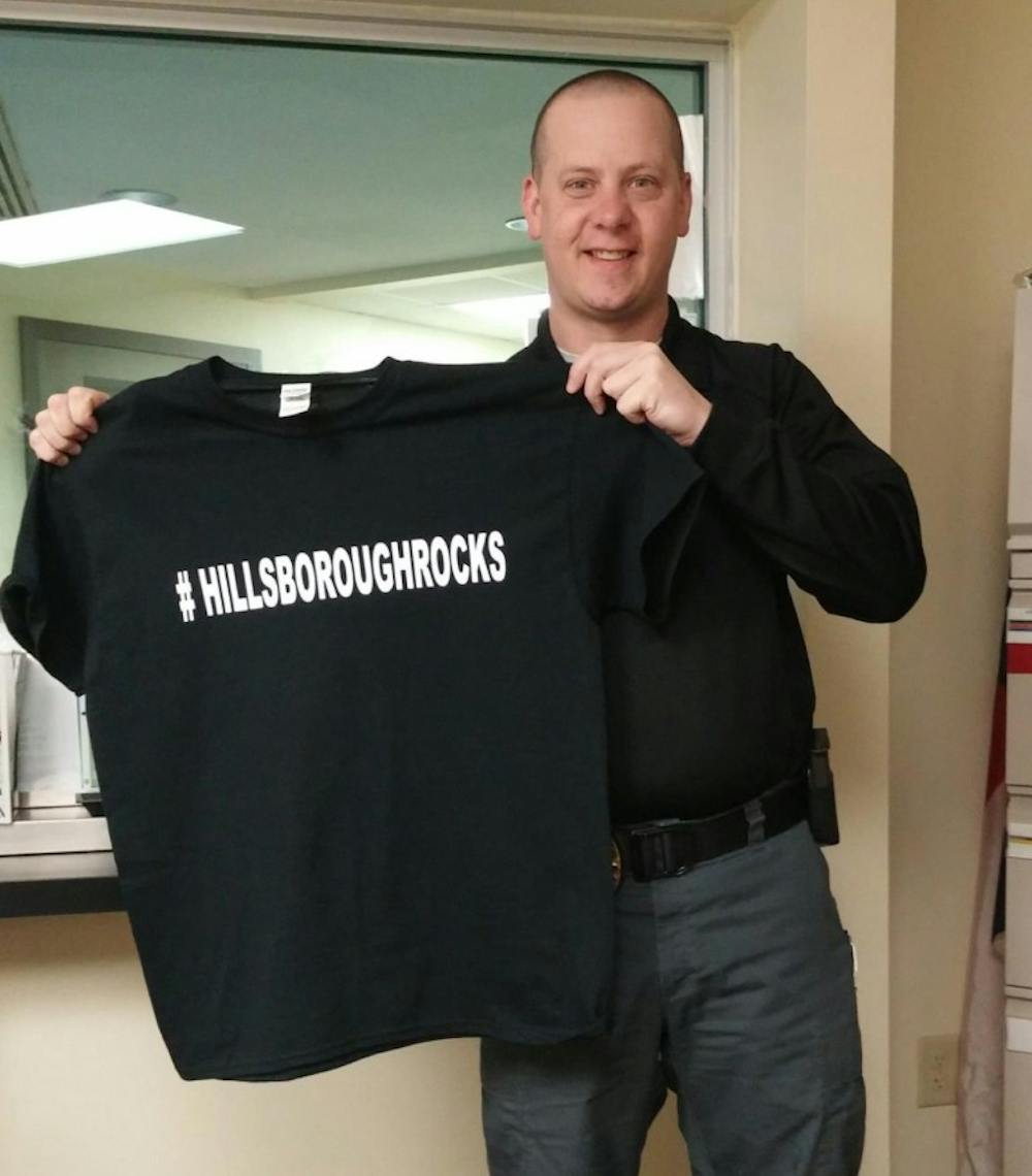<p>Hillsborough&nbsp;Lt. Andy Simmons holds up a t-shirt with the slogan "#HillsborouhgRocks" on it. Photo Courtesy of Lt. Andy Simmons.</p>
