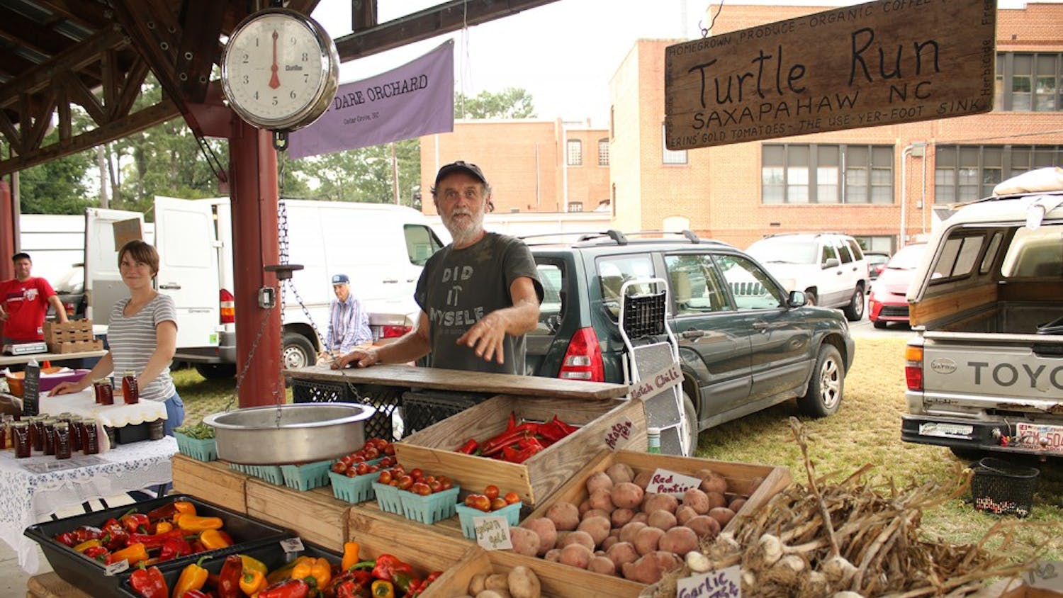 Kevin Meehan, a vendor at the Carrboro Farmer's Market, explains his scale at his booth. He sells homegrown produce from Turtle Run, his farm in Saxapahaw, NC.
