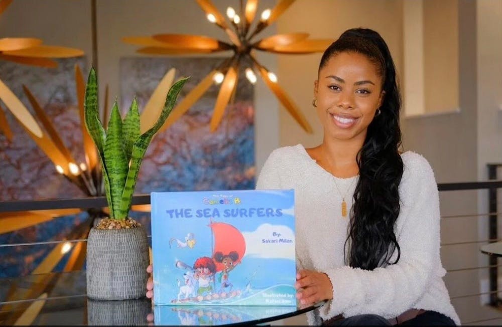 Sakari Milan, UNC alumna and author, with her book The Tales of Camelia B.: The Sea Surfers. Photo courtesy of Milan.