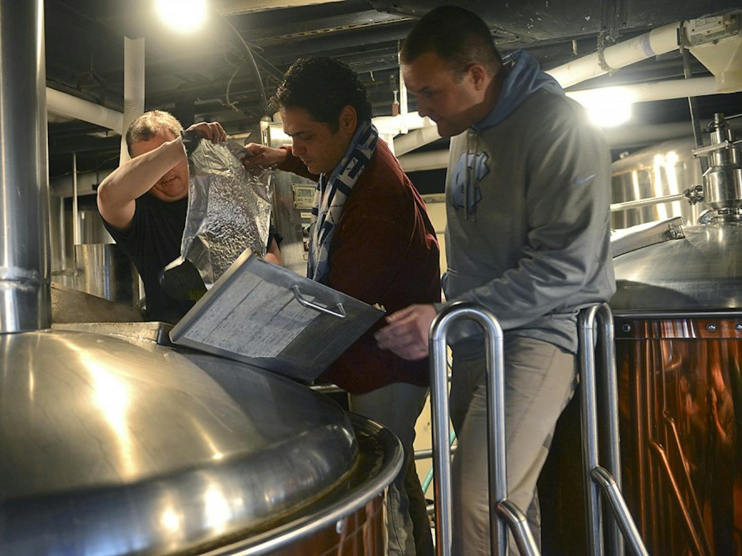 Chapel Hill mayor Mark Kleinschmidt pours hops into the Triangle Brewing Company's special game day brew for the first annual competition between the Top of the Hill and the Triangle Brewing Company Co-owner Rick Tufts (left) and co-brewmaster Aaron Caracci (right) supervise the process.