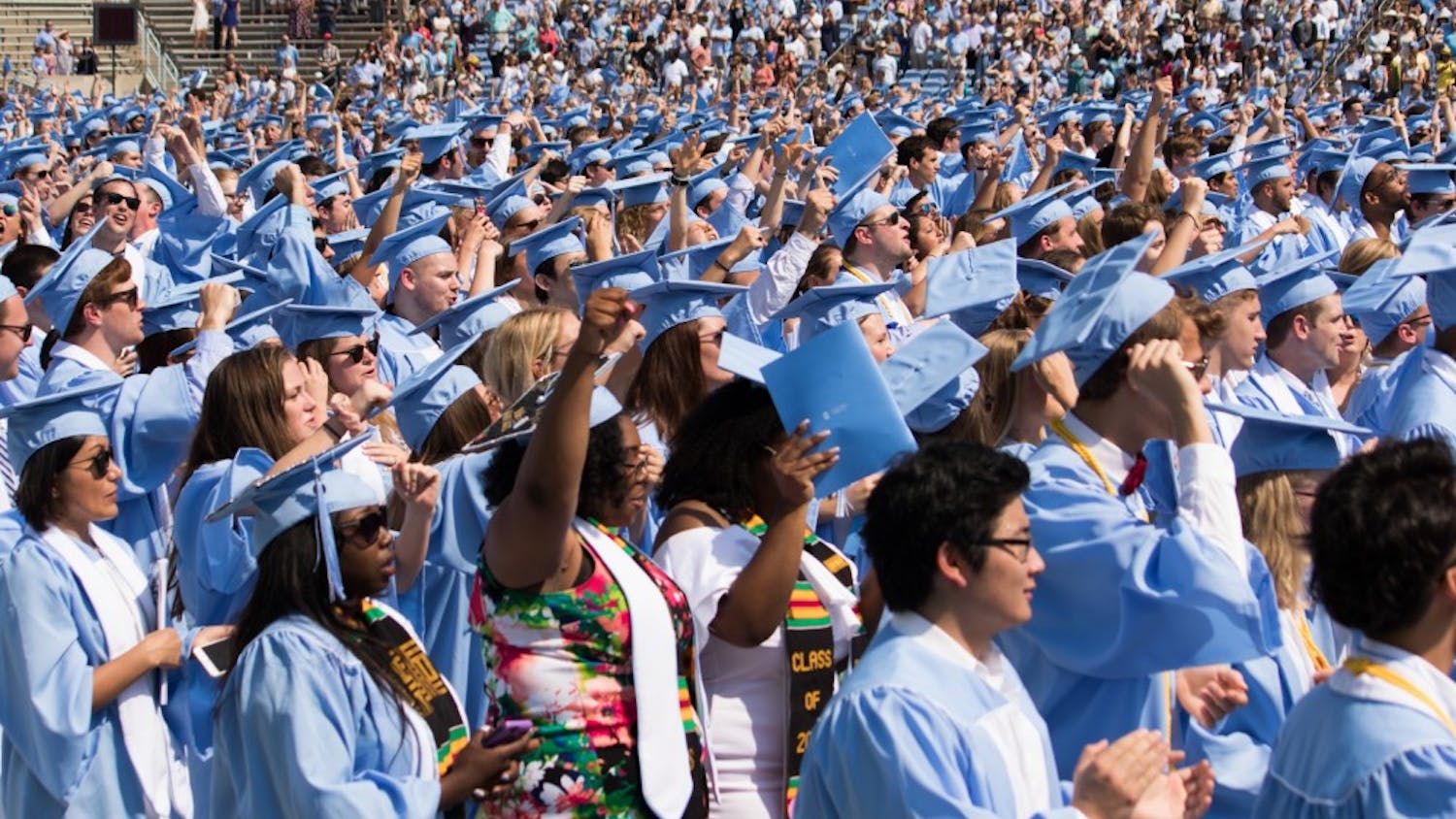 Students raise their fists at the end of "Hark the Sound" during Commencement on May 13.&nbsp;