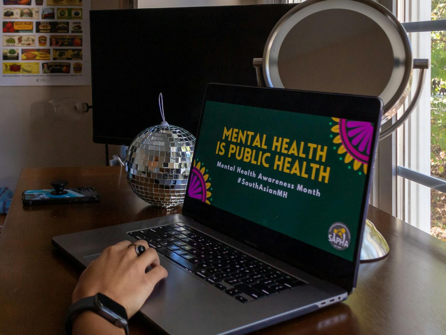 DTH Photo Illustration. A student views mental health facts on the South Asian Public Health Association website.