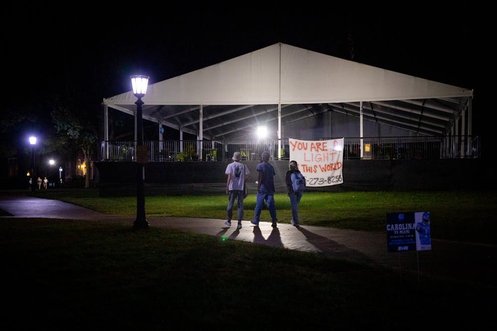 <p>Students walk across the quad on the evening of Thursday, Oct 14, 2021. Behind them, a banner offers support following the death of two UNC students by suicide that month.</p>