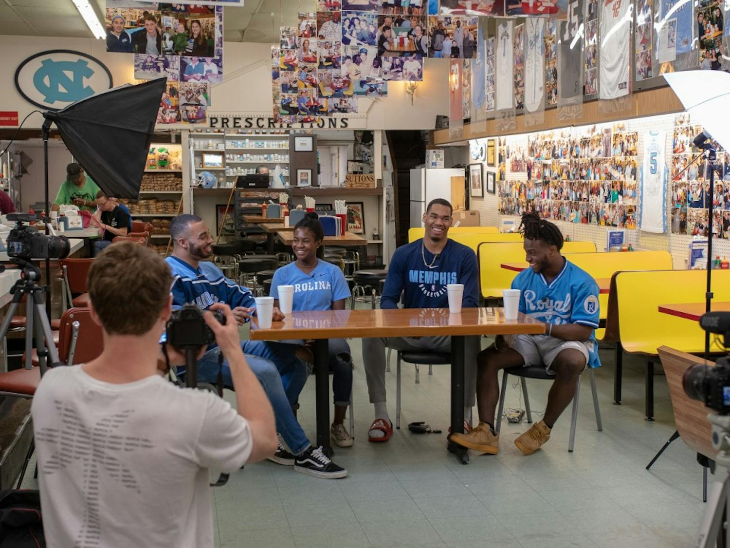 Sophomore Luke Buxton films as (from left to right) Jake Lawler, Brianna Pinto, Garrison Brooks and Michael Carter talk about life as black student-athletes at UNC for the student-produced show UNCUT filmed at Sutton's Drug Store.
Photo courtesy of Kenan Reed.