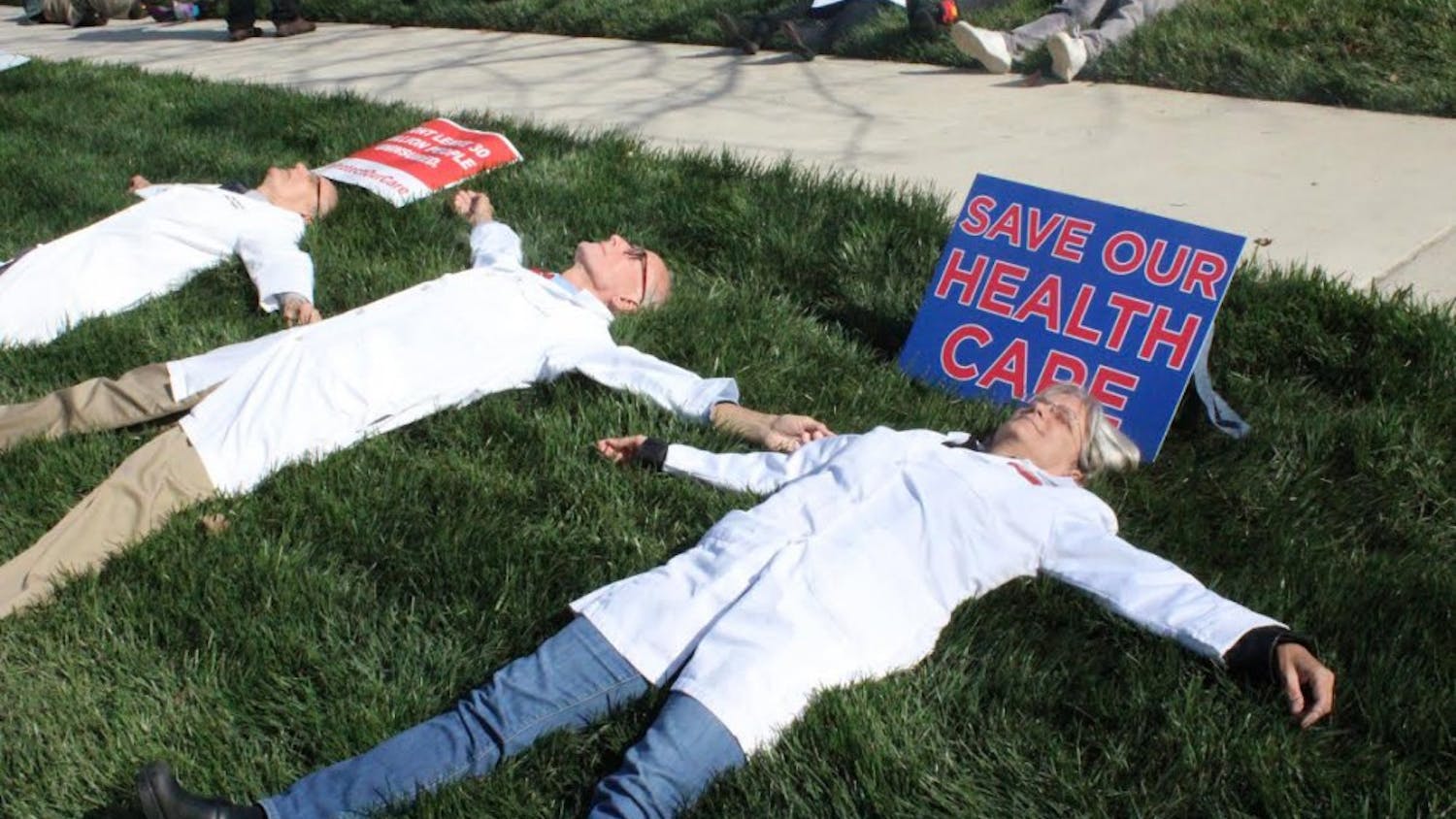 Participants spread out in the grass during Friday’s die-in in Durham in reaction to the possible changes in health care policies.