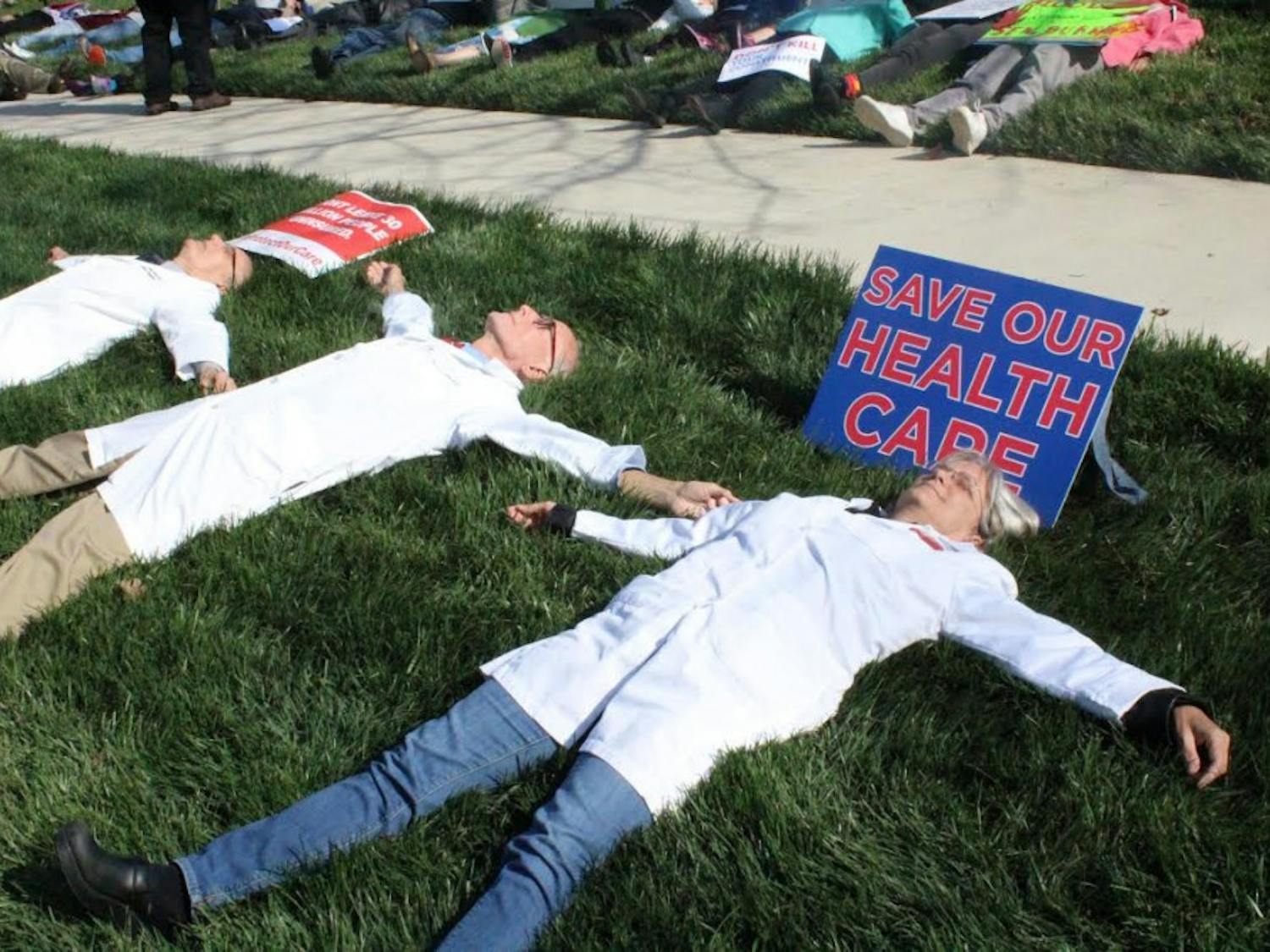 Participants spread out in the grass during Friday’s die-in in Durham in reaction to the possible changes in health care policies.