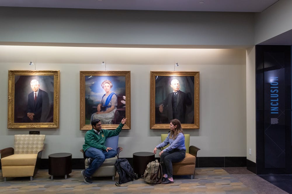 <p>Kerry McIntyre and Rohit Sharma, students of the MBA class of 2023, engage in conversation in the lobby of McColl Building on Monday, Oct. 3, 2022. Hanging behind them are the portraits of Hugh L. McColl, Jr., Mary Lily Kenan, and Henry Flagler, the namesakes of &nbsp;McColl Building and Kenan-Flagler Business School.</p>